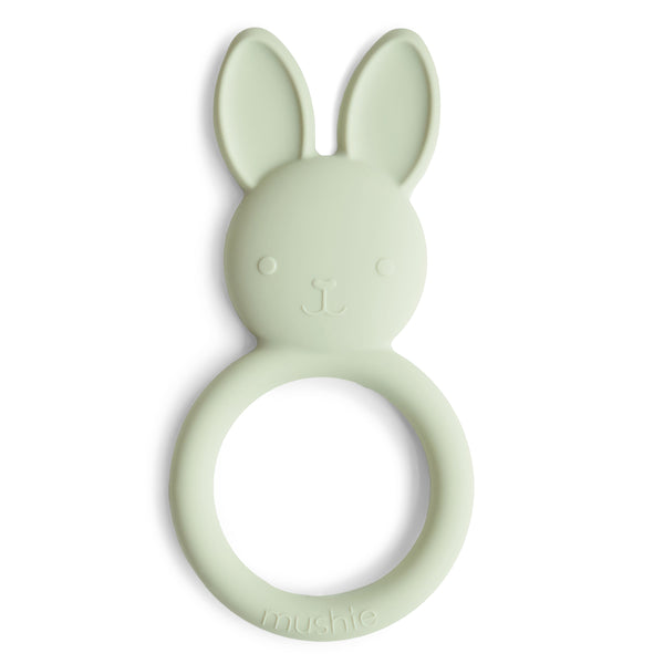 The mushie Bunny Teether is a pale green, non-toxic silicone teether shaped like a bunny head with large ears, a circular handle embossed with "mushie," and a cute face—perfectly safe for babies.